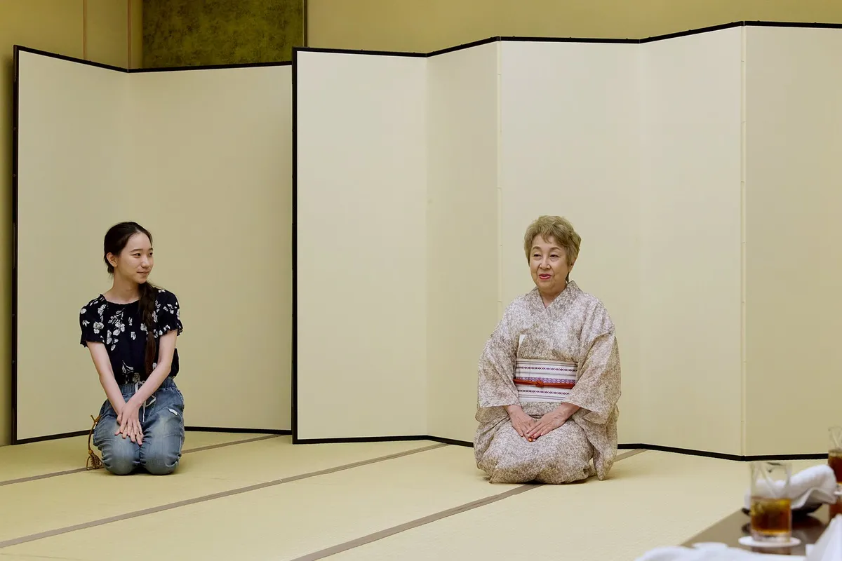 屏風の前の畳に座って話す女将と、少し離れて座るお客様。