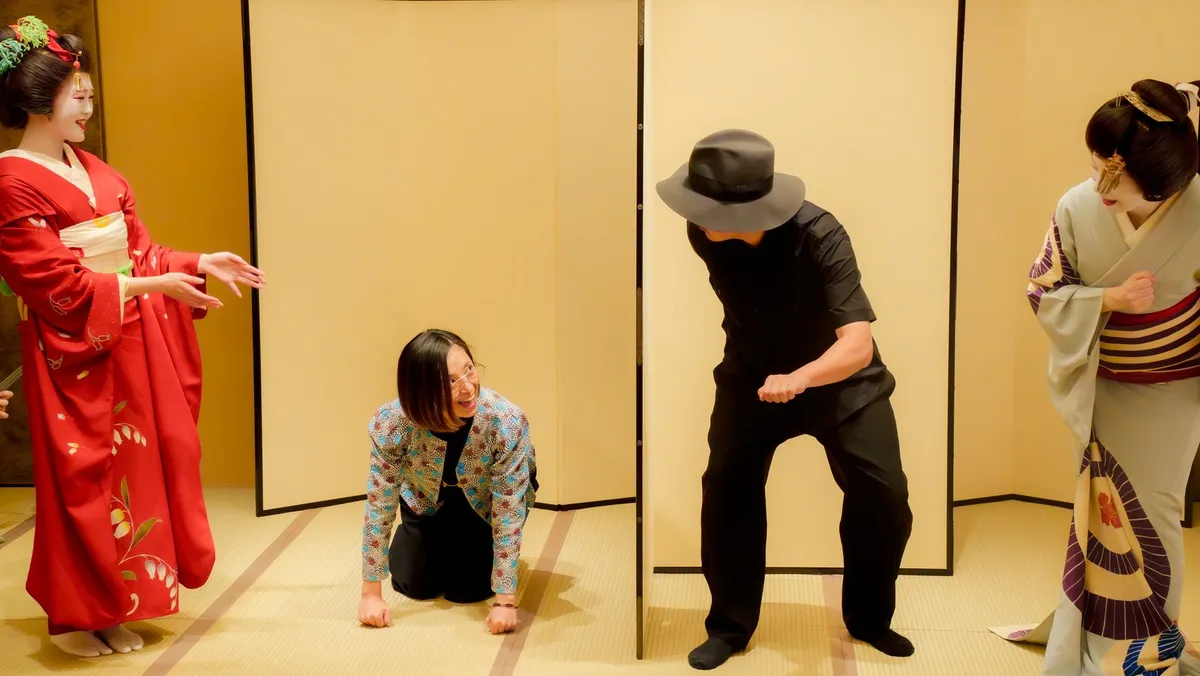 屏風の前で、とらとらの姿を決めるお客様二人と、両脇でそれを見る芸者衆。