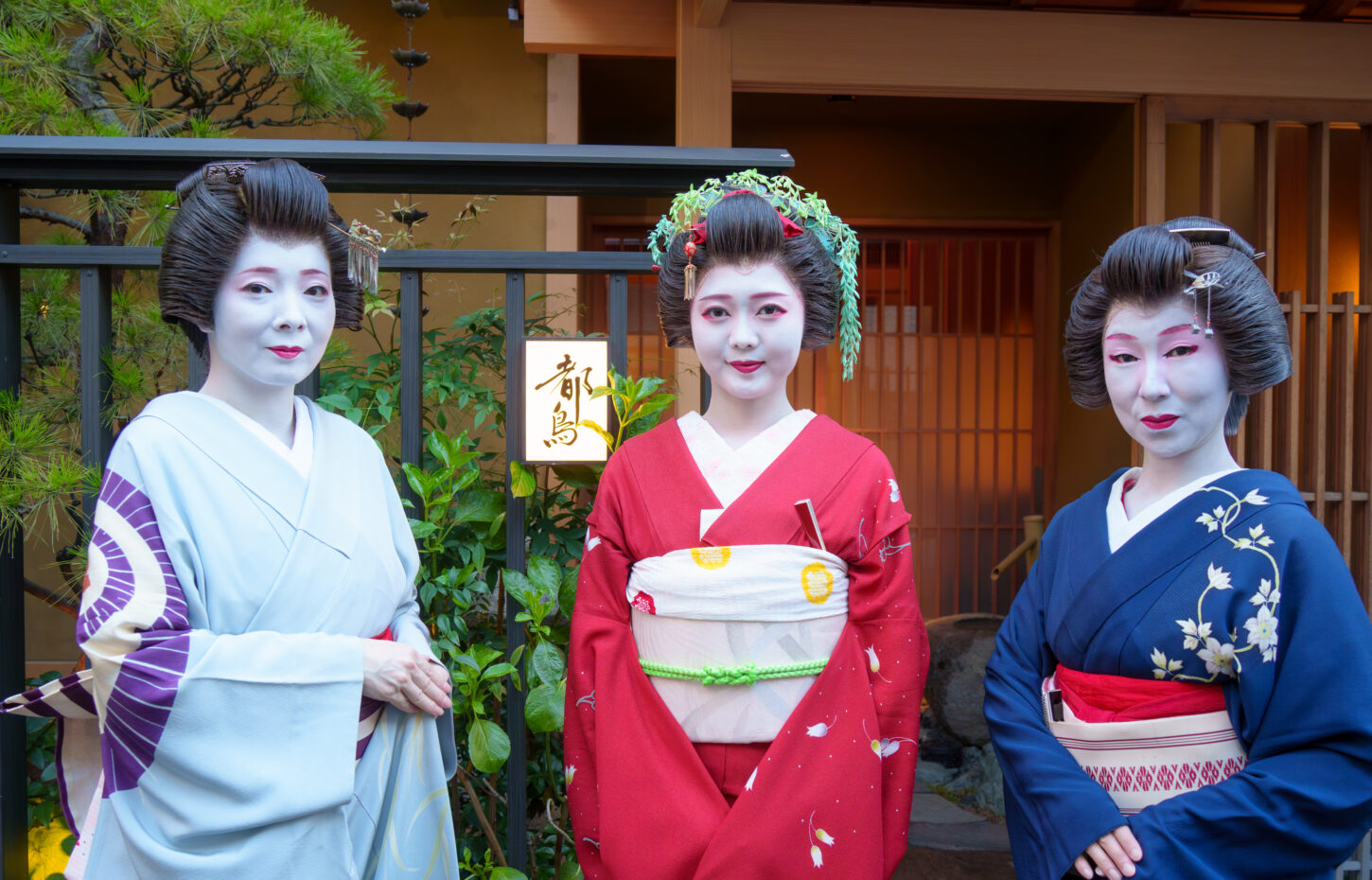 都鳥の店先に立つ芸者衆3名。中央に半玉、奥に「都鳥」の行灯が灯る
