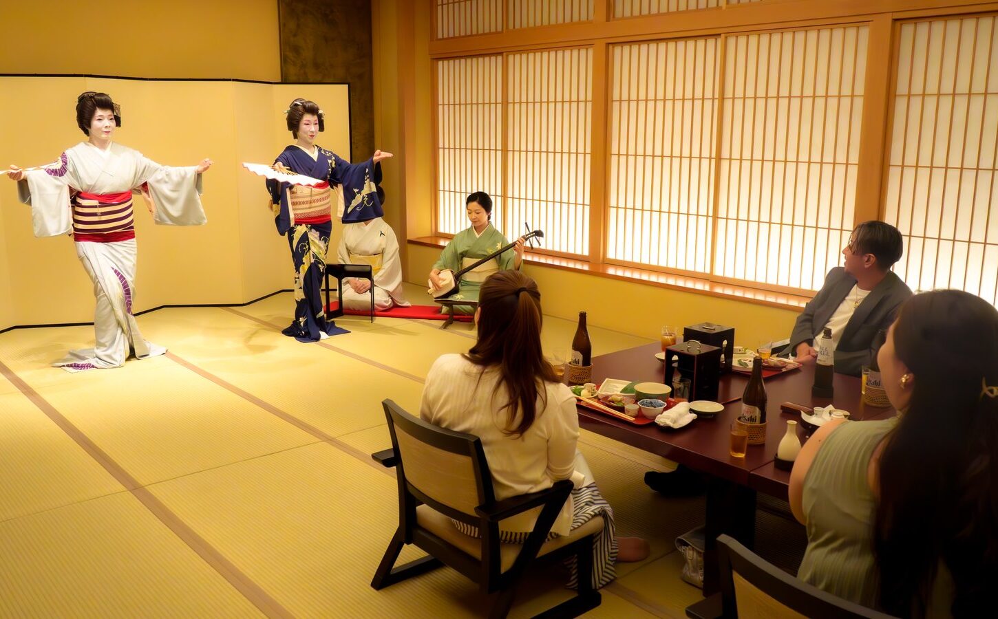 都鳥のお座敷(宴の最中) - 浅草 都鳥 浅草 都鳥のお座敷。屏風の前で芸者衆2名が扇を手に舞い、三味線に合わせてお客様が膳を前に見ている