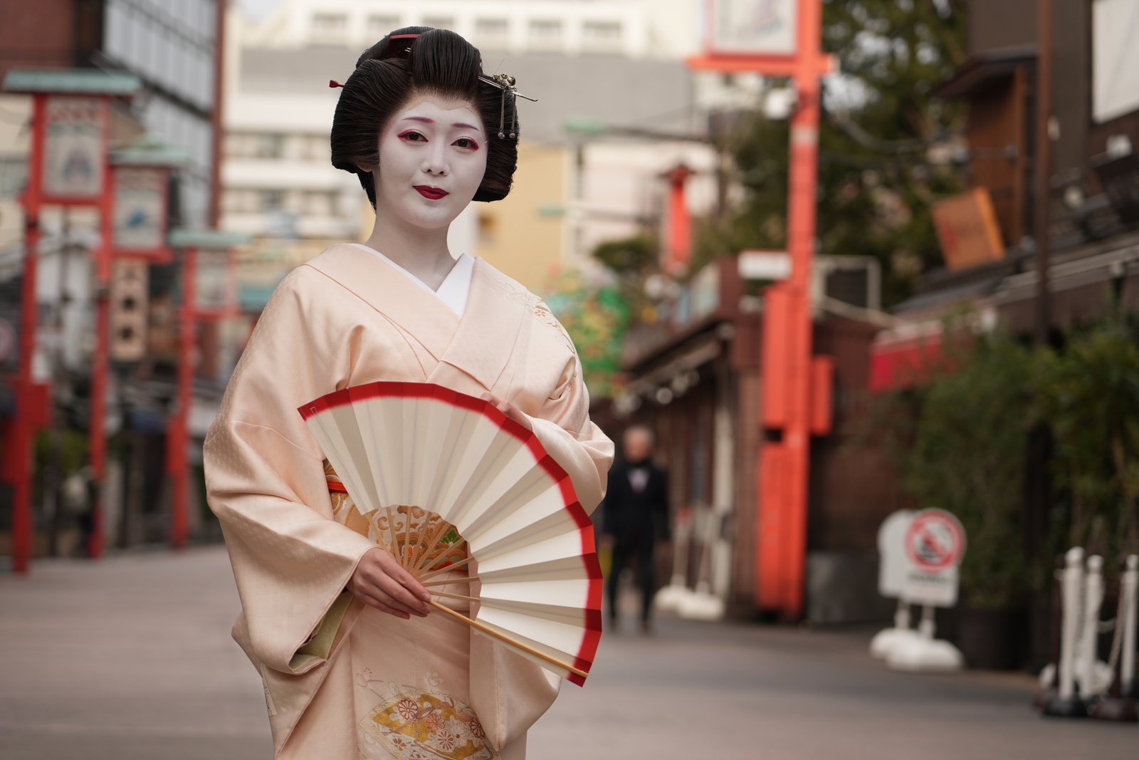 浅草の街に立つ芸者 浅草の通りに立つ芸者。昼の自然光のなか、着物姿で扇を持っている