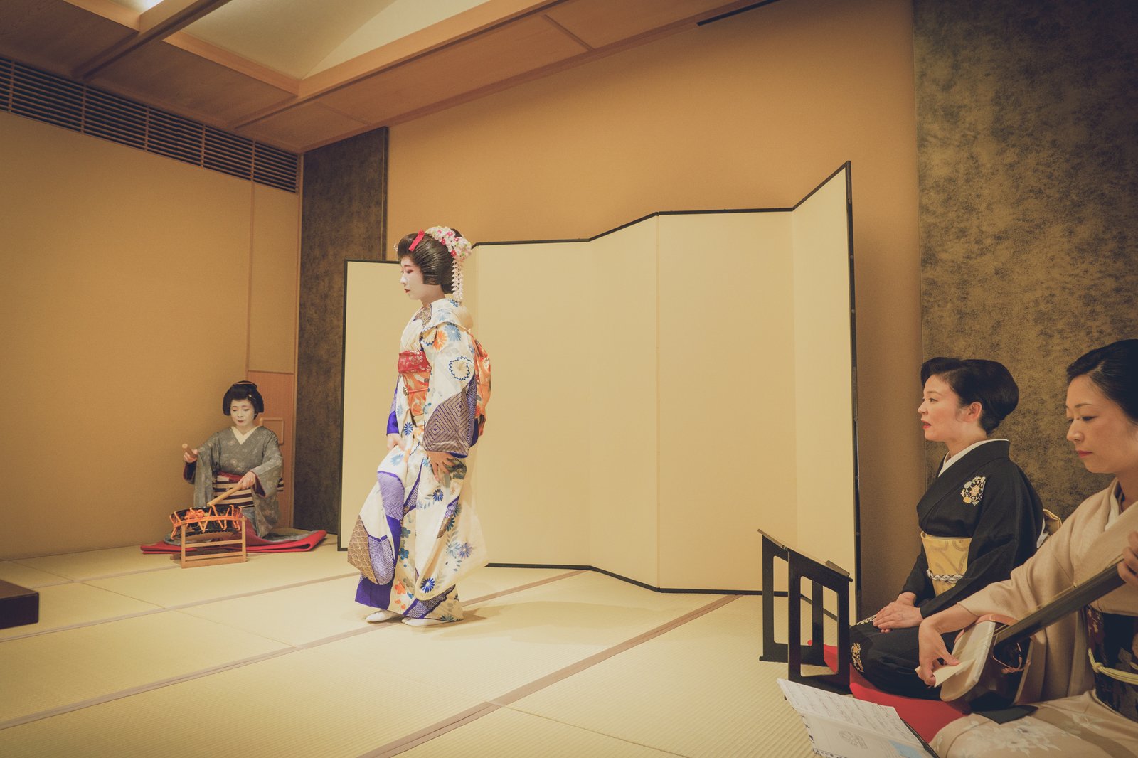 屏風の前で扇を手に舞う浅草の芸者。奥に地方（じかた）が控える