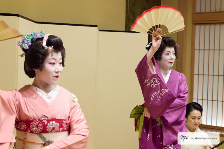 扇を掲げて舞う芸者と、手前の芸者